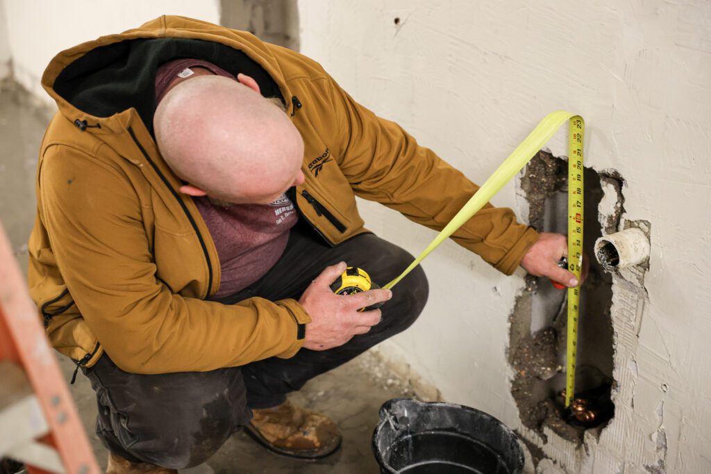 HVAC technician measuring space for commercial pipe installation as part of commercial HVAC & plumbing maintenance